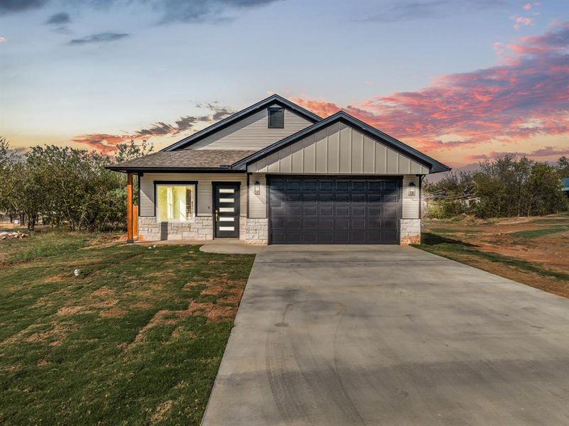 View of front of property with concrete driveway, stone siding, board and batten siding, a garage, and a front lawn View of front of property with concrete driveway, stone siding, board and batten siding, a garage, and a front lawn