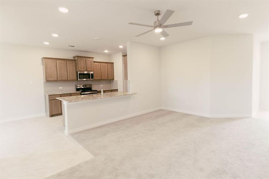 Kitchen featuring ceiling fan, light stone counters, appliances with stainless steel finishes, kitchen peninsula, and backsplash