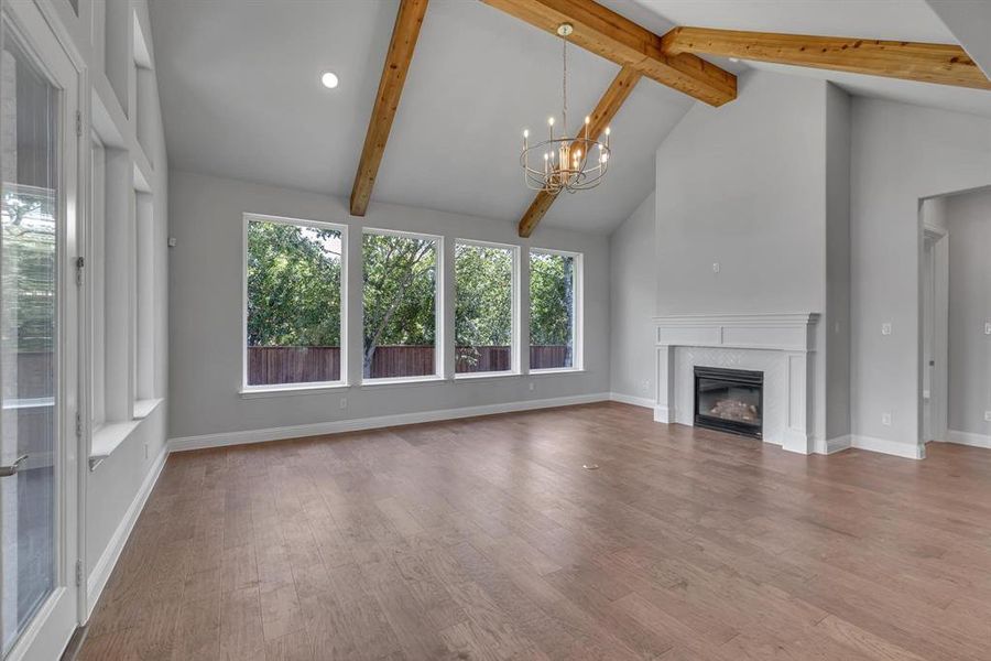 Unfurnished living room with high vaulted ceiling, wood-type flooring, an inviting chandelier, and beamed ceiling