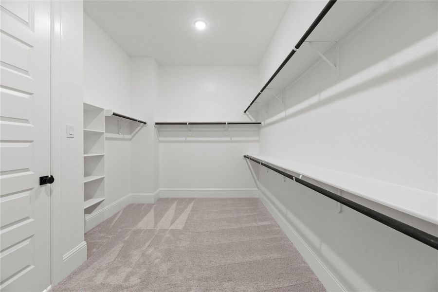 The primary closet offers ample storage with double hanging rods, built-in shelving, and plush carpeting.