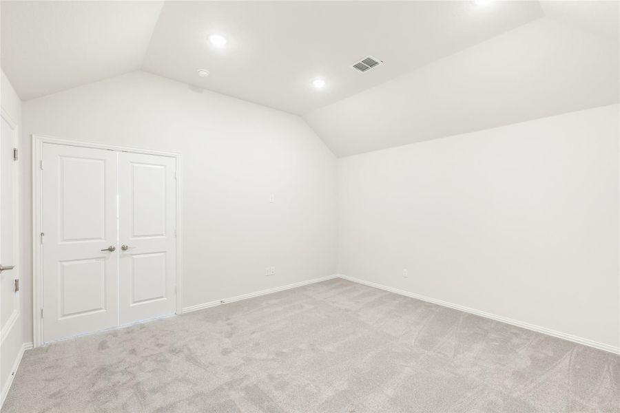 Empty bedroom with vaulted ceiling, gray carpet, and double closet doors