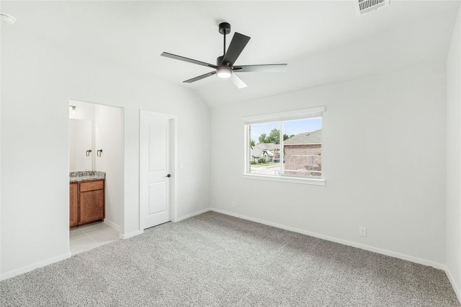 Bedroom with vaulted ceiling, ceiling fan, carpet flooring, and ensuite bathroom access