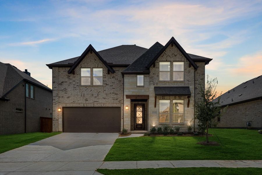 Two-story brick home with dark roof, two-car garage, and front lawn at dusk