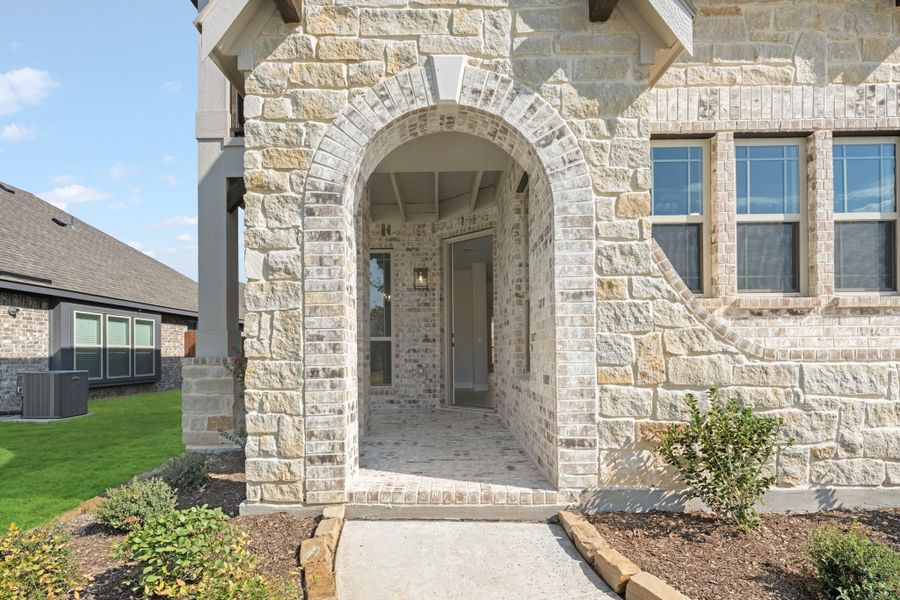 Stone home entrance with arched doorway, brick and limestone exterior, and covered front porch