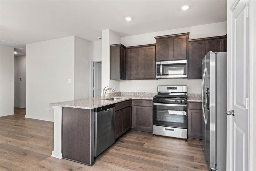 Kitchen featuring stainless steel appliances, dark brown cabinets, light stone countertops, recessed lighting, and dark wood-style floors