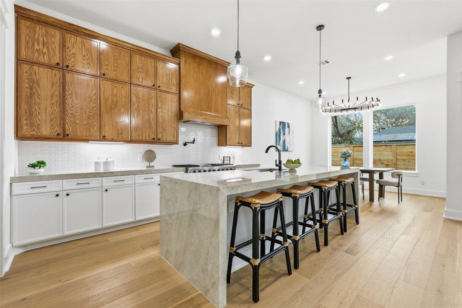 A striking waterfall porcelain island anchors the kitchen, complemented by white oak upper cabinetry and crisp solid-wood lower cabinets. The result is a space that blends refined craftsmanship with warm, livable elegance.