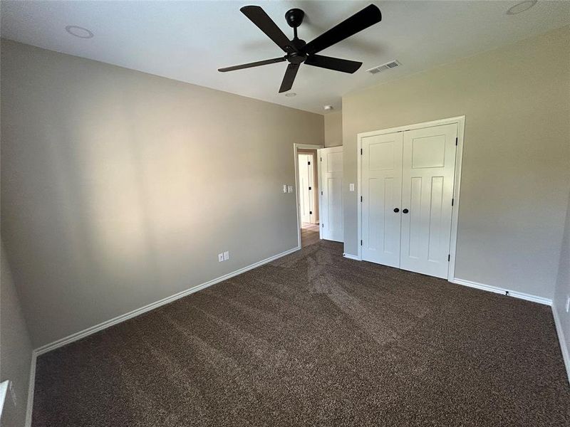 Unfurnished bedroom featuring dark colored carpet, a closet, and a ceiling fan