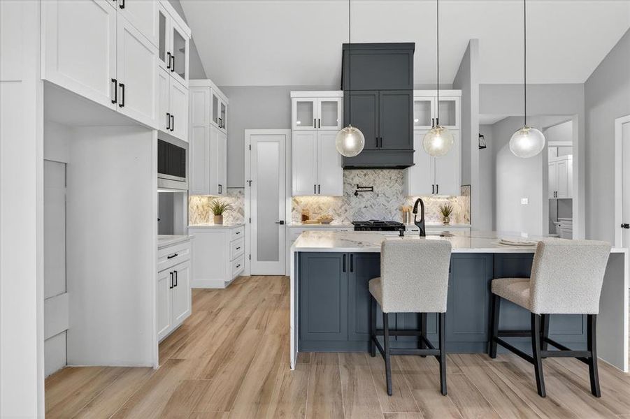 Modern kitchen featuring a two-tone design with white upper cabinetry and dark blue lower cabinetry, a center island with countertop seating, wood-finish flooring, and pendant lighting