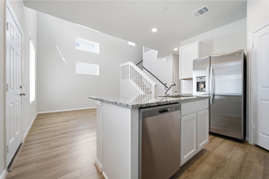 Kitchen with stainless steel appliances, white cabinets, an island with sink, light stone countertops, and light wood-style floors