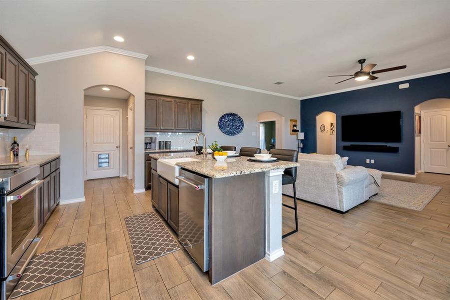 Kitchen featuring arched walkways, light stone countertops, ornamental molding, a kitchen breakfast bar, and open floor plan