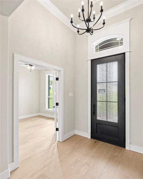 Foyer with light wood-style floors, a chandelier, a towering ceiling, and crown molding Foyer with light wood-style floors, a chandelier, a towering ceiling, and crown molding