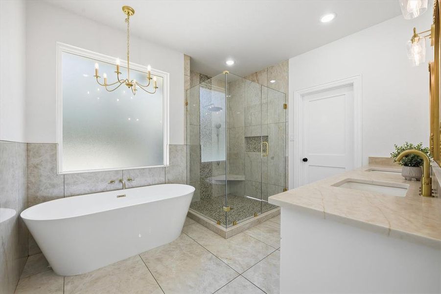 Full bathroom featuring a soaking tub, a stall shower, double vanity, tile walls, and suspended lighting