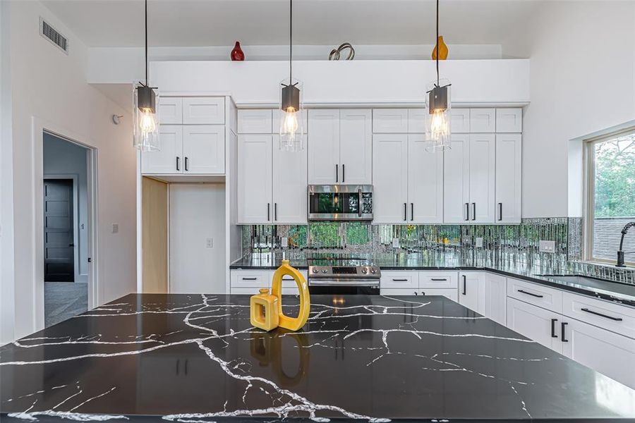 Modern kitchen featuring white cabinetry, sleek black countertops with dramatic veining, and stylish pendant lighting. The space is bright, with a glass tile backsplash enhancing its contemporary appeal.