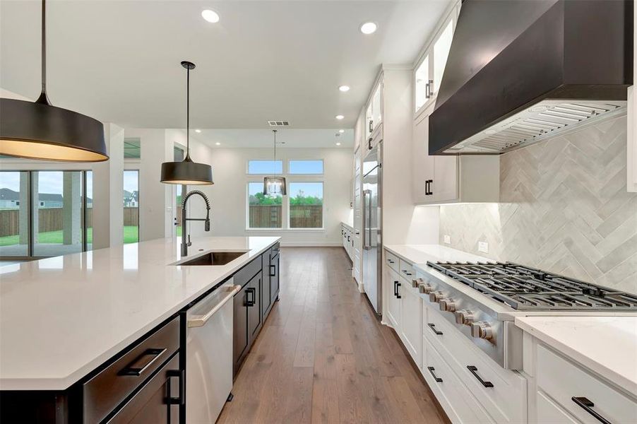 Dual tone kitchen featuring dual tone cabinetry, stainless steel appliances, a spacious island, light wood finished floors, and light stone countertops