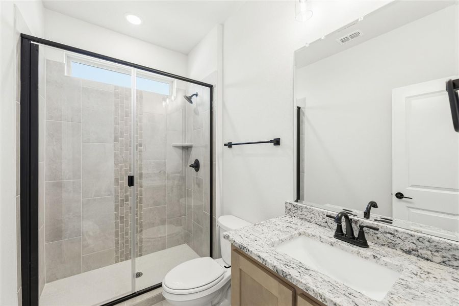 Bathroom with glass-enclosed tile shower, granite vanity countertop, and black fixtures