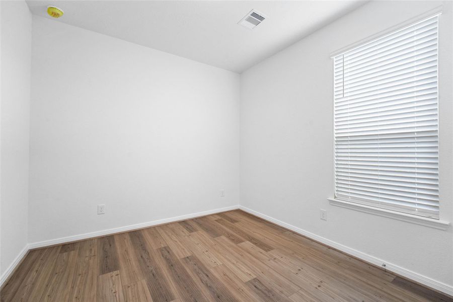 Secondary bedroom features Bandera vinyl plank flooring, neutral paint, lighting, large window with privacy blinds, and an ample sized closet space.