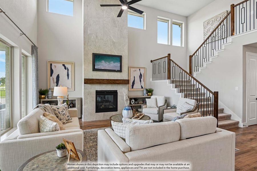 Living room with two-story ceiling, floor-to-ceiling stone fireplace, ceiling fan, and staircase with metal railings Living room with two-story ceiling, floor-to-ceiling stone fireplace, ceiling fan, and staircase with metal railings
