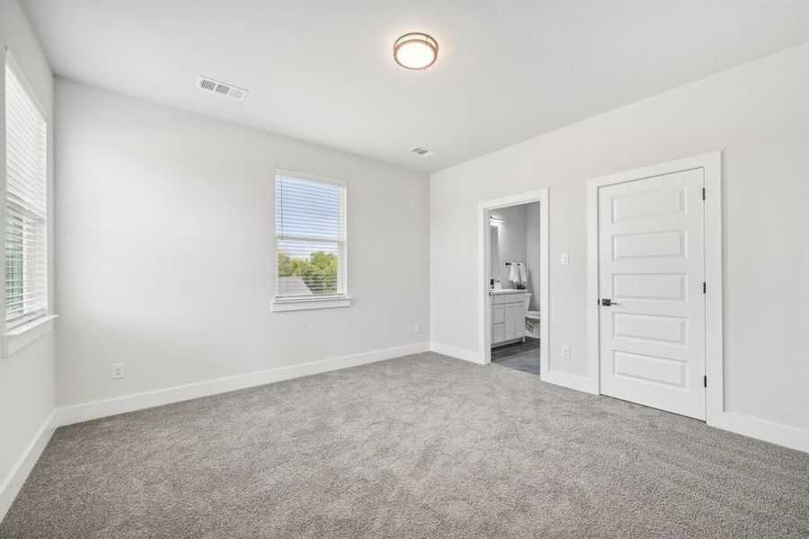 Unfurnished bedroom featuring connected bathroom, dark colored carpet, and a closet