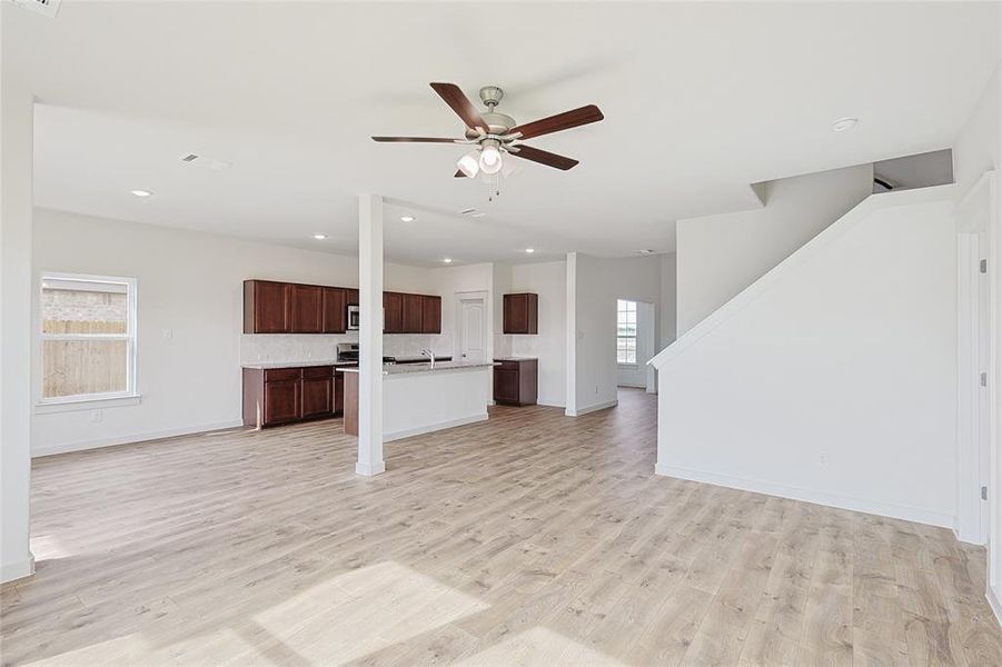 Unfurnished living room with light wood-type flooring, ceiling fan, and a healthy amount of sunlight