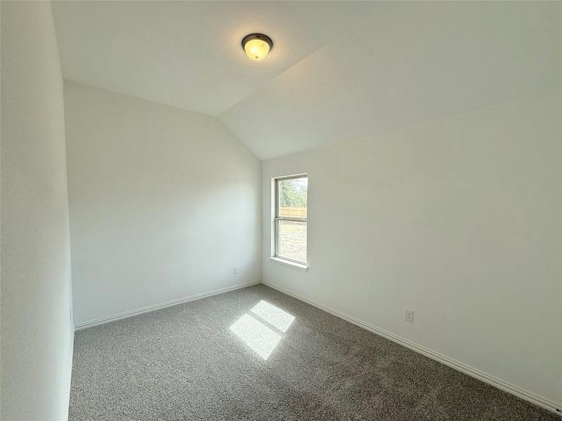 Carpeted spare room with vaulted ceiling and baseboards Carpeted spare room with vaulted ceiling and baseboards