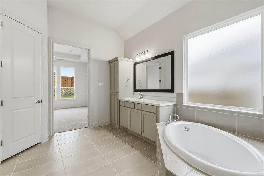 Bathroom featuring vanity, light tile patterned floors, a bath, and vaulted ceiling