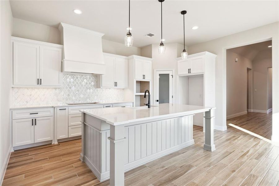 Kitchen featuring sink, pendant lighting, a center island with sink, stovetop, and white cabinetry