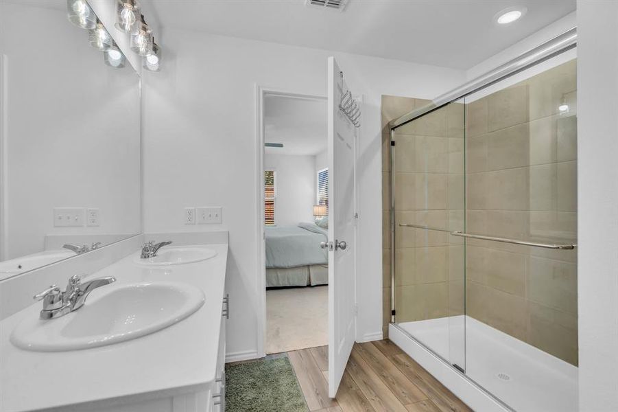 Ensuite bathroom featuring light wood-type flooring, a shower stall, double vanity, and recessed lighting