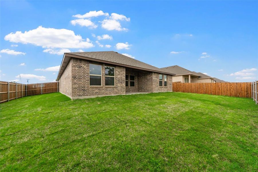 Expansive rear lawn featuring a privacy fence, brick exterior, and covered patio