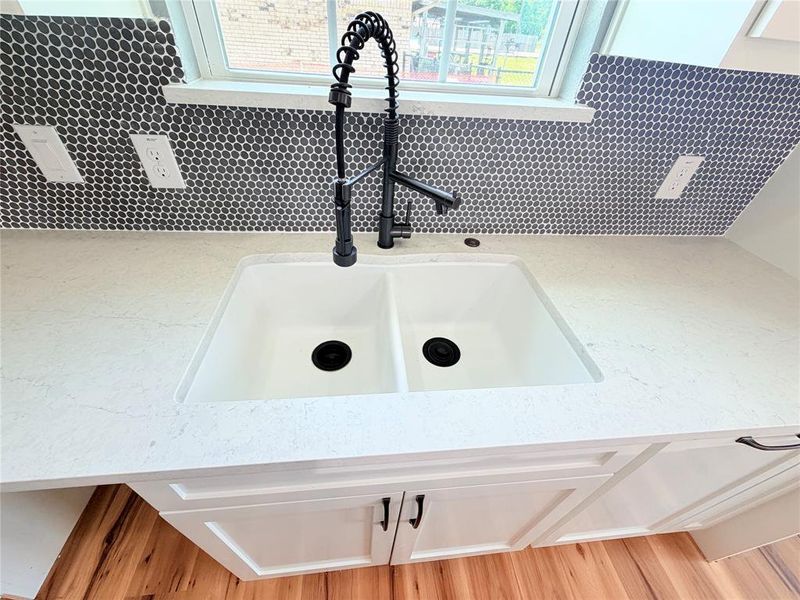 Kitchen sink area featuring a dual-basin sink, white countertops, and dark penny tile backsplash