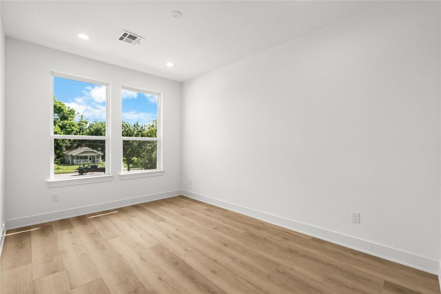 The third bedroom features light oak flooring, smooth white walls, and two large windows with views of mature trees and greenery. The bright, peaceful layout works perfectly as either a bedroom or a home office.