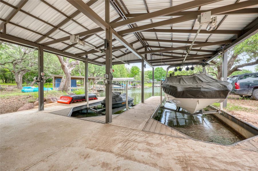 Covered boat dock featuring a metal roof structure, two boat lifts, a concrete walkway, and direct water access