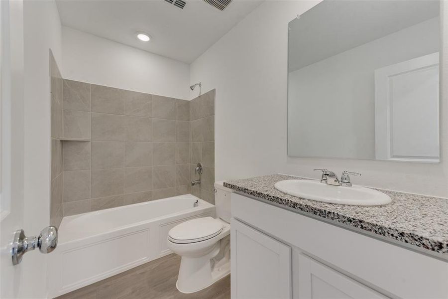 Full bathroom featuring vanity, toilet, tiled shower / bath combo, and hardwood / wood-style floors