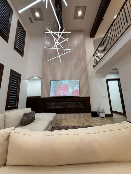 Living area with arched walkways, a glass covered fireplace, a towering ceiling, and beam ceiling
