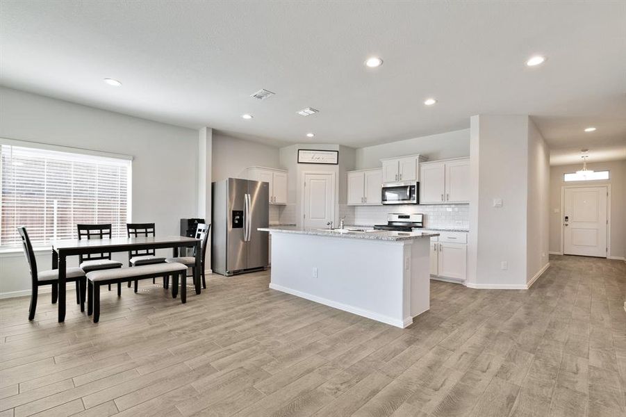 Kitchen with decorative backsplash, stainless steel appliances, white cabinetry, an island with sink, and light stone counters
