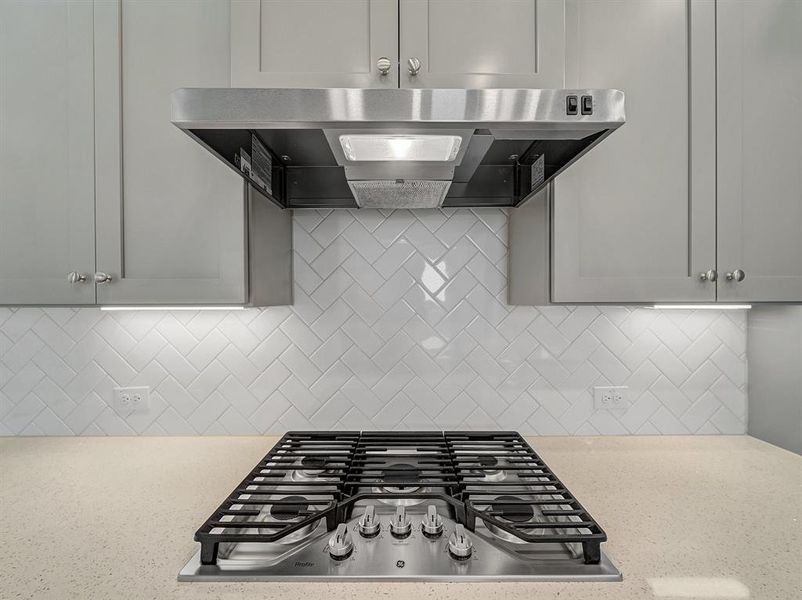 Kitchen featuring ventilation hood, light stone counters, tasteful backsplash, and stainless steel gas stovetop