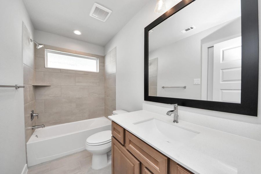 Secondary bath features tile flooring, bath/shower combo with tile surround, light stained wood cabinets, beautiful light countertop. Sample photo of completed home with similar floor plan. Actual colors and selections may vary. Secondary bath features tile flooring, bath/shower combo with tile surround, light stained wood cabinets, beautiful light countertop. Sample photo of completed home with similar floor plan. Actual colors and selections may vary.