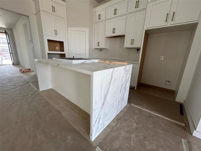 The open white kitchen exudes a sense of airy elegance, with pristine cabinets and countertops gleaming under the soft glow of recessed lighting.