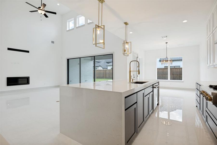 Spacious kitchen and living area featuring a large center island with an undermount sink and gold-tone faucet, white cabinetry, and gleaming tile flooring Spacious kitchen and living area featuring a large center island with an undermount sink and gold-tone faucet, white cabinetry, and gleaming tile flooring
