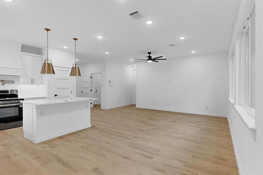 Kitchen with stainless steel range, white cabinetry, pendant lighting, a kitchen island, and light wood-type flooring Kitchen with stainless steel range, white cabinetry, pendant lighting, a kitchen island, and light wood-type flooring