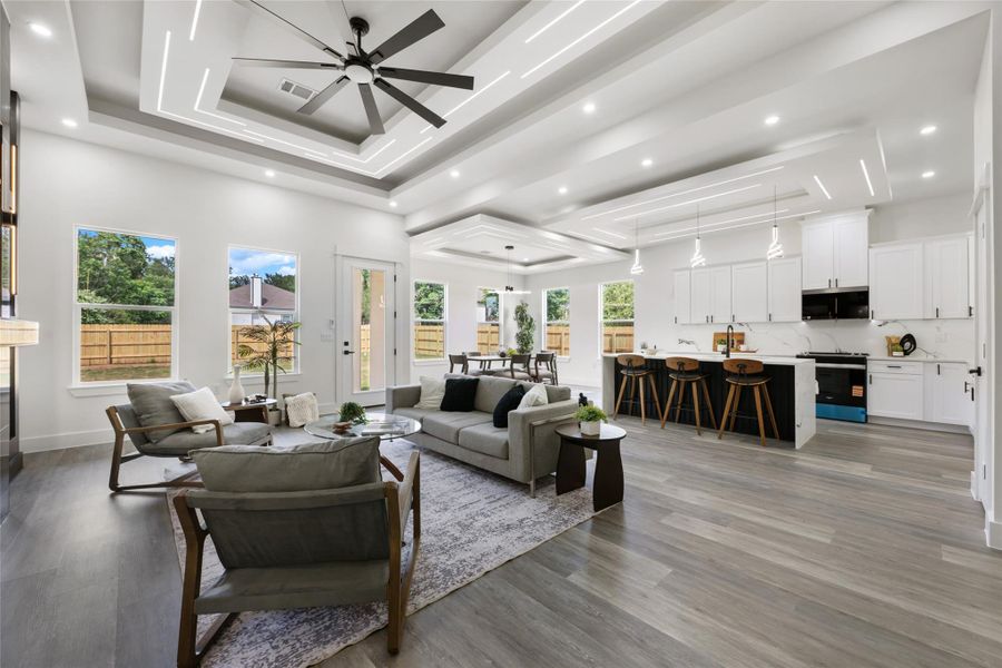 Open-concept living area featuring a multi-tiered tray ceiling with integrated lighting, wood-finish flooring, and multiple windows