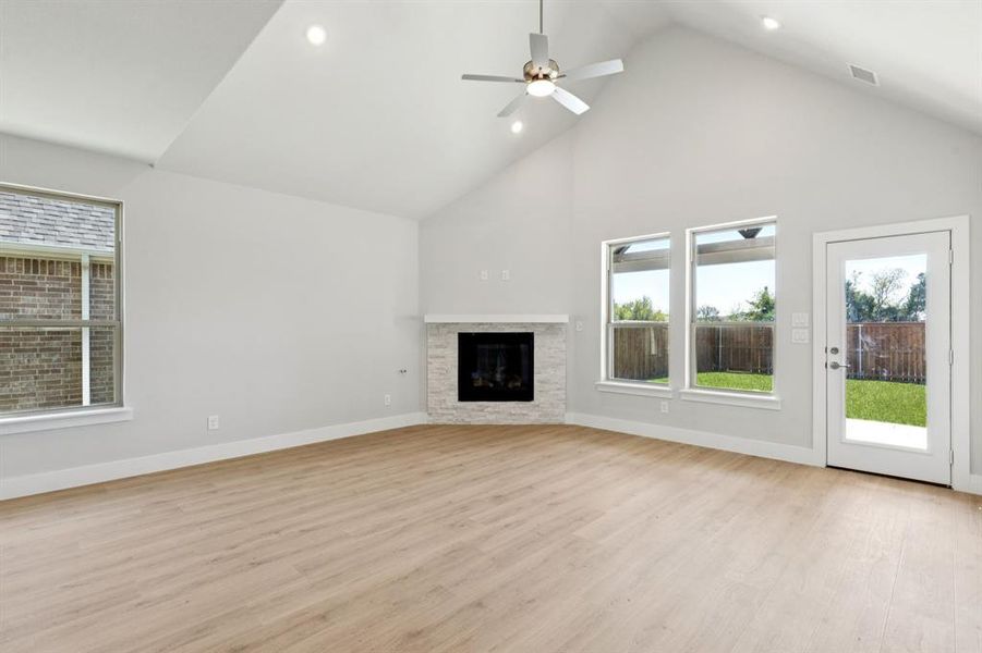 Unfurnished living room featuring plenty of natural light, recessed lighting, high vaulted ceiling, light wood-style floors, and a stone fireplace Unfurnished living room featuring plenty of natural light, recessed lighting, high vaulted ceiling, light wood-style floors, and a stone fireplace