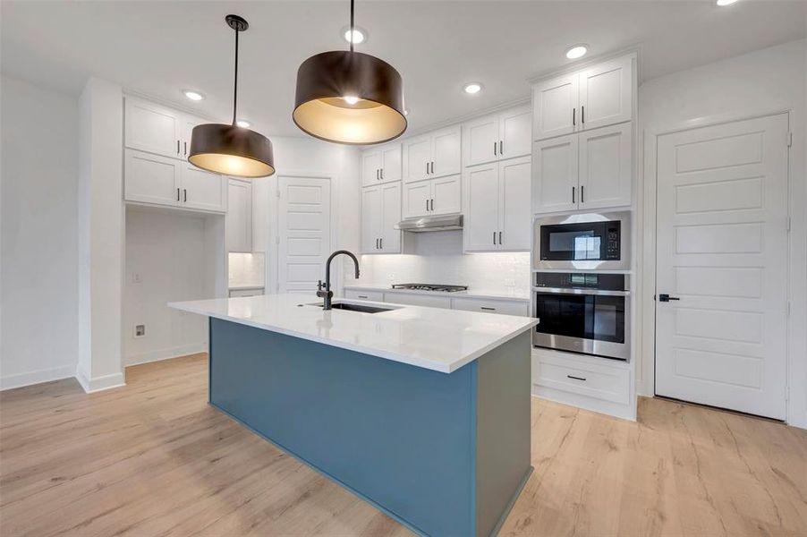 Contemporary kitchen featuring a prominent island with a white countertop and dark blue base, complemented by two large pendant lights Contemporary kitchen featuring a prominent island with a white countertop and dark blue base, complemented by two large pendant lights