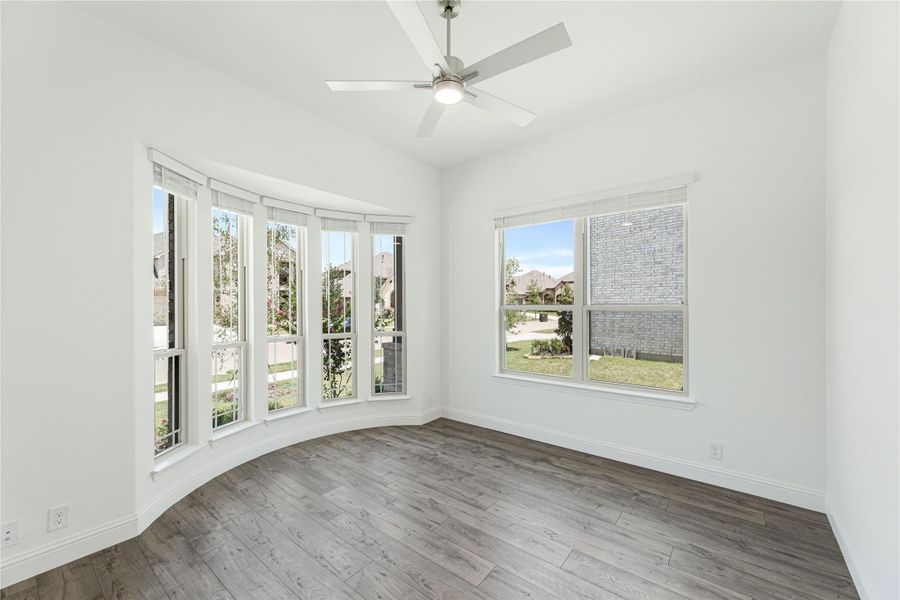 Empty room with bay windows, ceiling fan, and gray hardwood floors Empty room with bay windows, ceiling fan, and gray hardwood floors