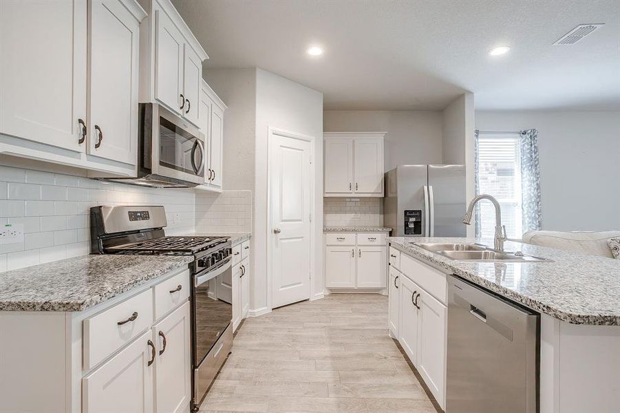 Kitchen with stainless steel appliances, white cabinetry, light wood-style floors, a center island with sink, and light stone countertops