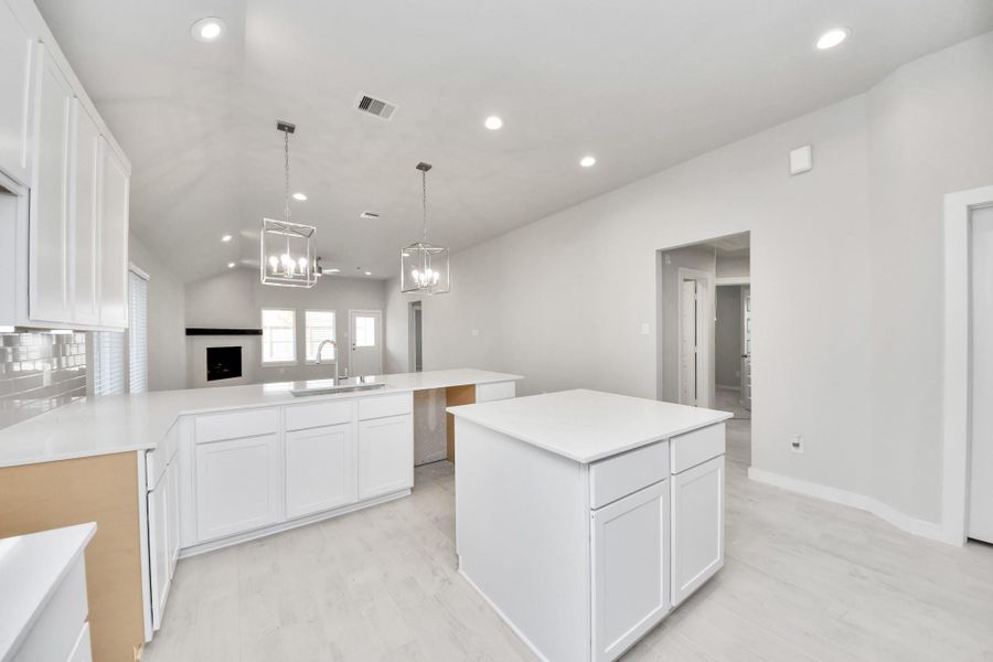 This kitchen is truly a chef's dream! This haven Boasts high ceilings, recessed & pendant lighting, stained wood cabinets, granite countertops, stainless steel appliances, a modern tile backsplash.  All of this overlooks your expansive family room, creating a perfect space for culinary delights and family gatherings. Sample photo of completed home with similar floor plan. Actual colors and selections may vary.