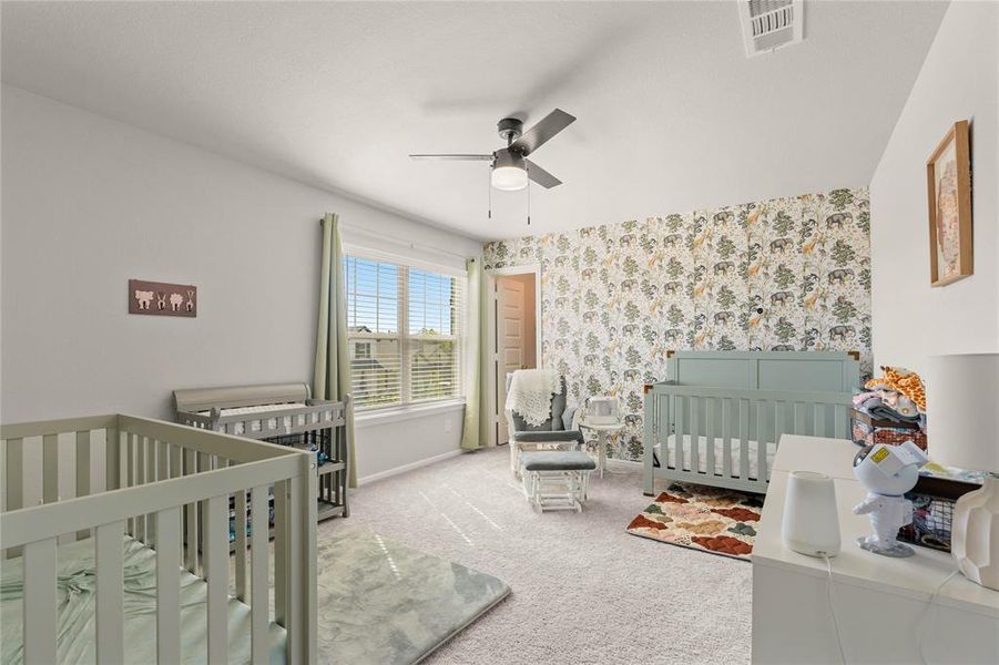 Upstairs carpeted bedroom featuring a crib, wallpapered walls, walk-in closet and ceiling fan