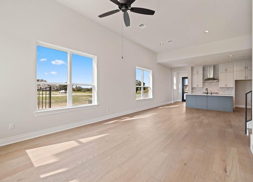 Unfurnished living room featuring a wealth of natural light, visible vents, light wood-type flooring, and a ceiling fan Unfurnished living room featuring a wealth of natural light, visible vents, light wood-type flooring, and a ceiling fan