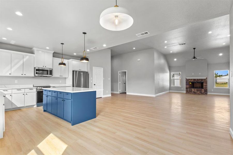 Kitchen with white cabinets, hanging light fixtures, a fireplace, stainless steel appliances, and open floor plan