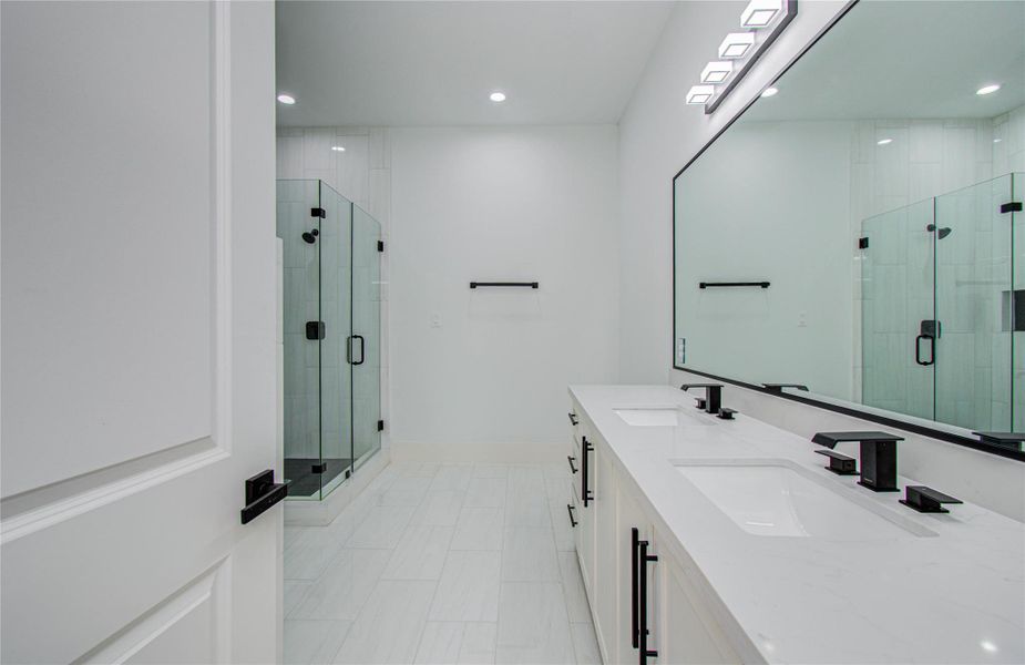 This primary en-suite bathroom features a modern design with dual sinks, sleek black fixtures, and a large mirror. It includes a spacious glass-enclosed shower, freestanding soaking tub, and bright, modern design.