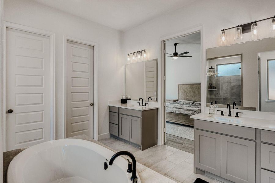 Ensuite bathroom featuring two vanities, light tile patterned floors, a bath, and a ceiling fan